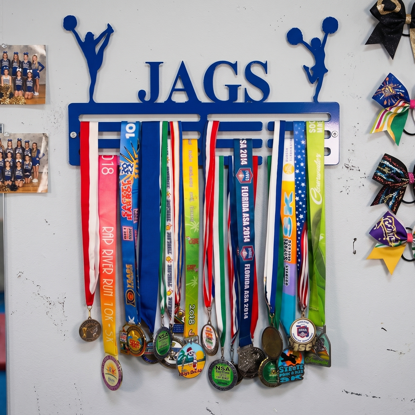 Medal holder with 'JAGS' on a white wall with various medals hanging from it. Cheerleader Medal and Award Hanger.  Cheer Award Display