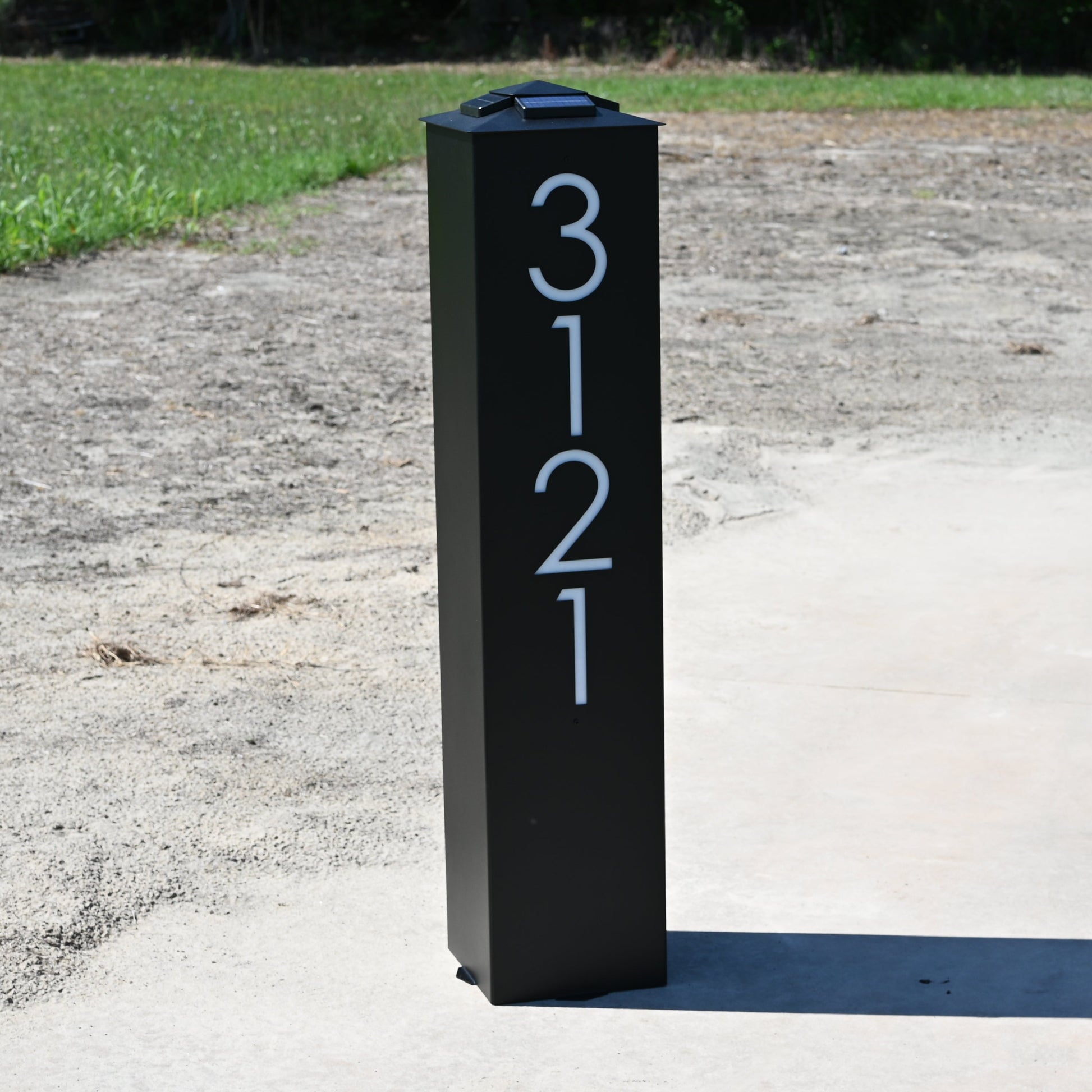 Black post with numbers '3121' on a dirt path with grass and trees in the background