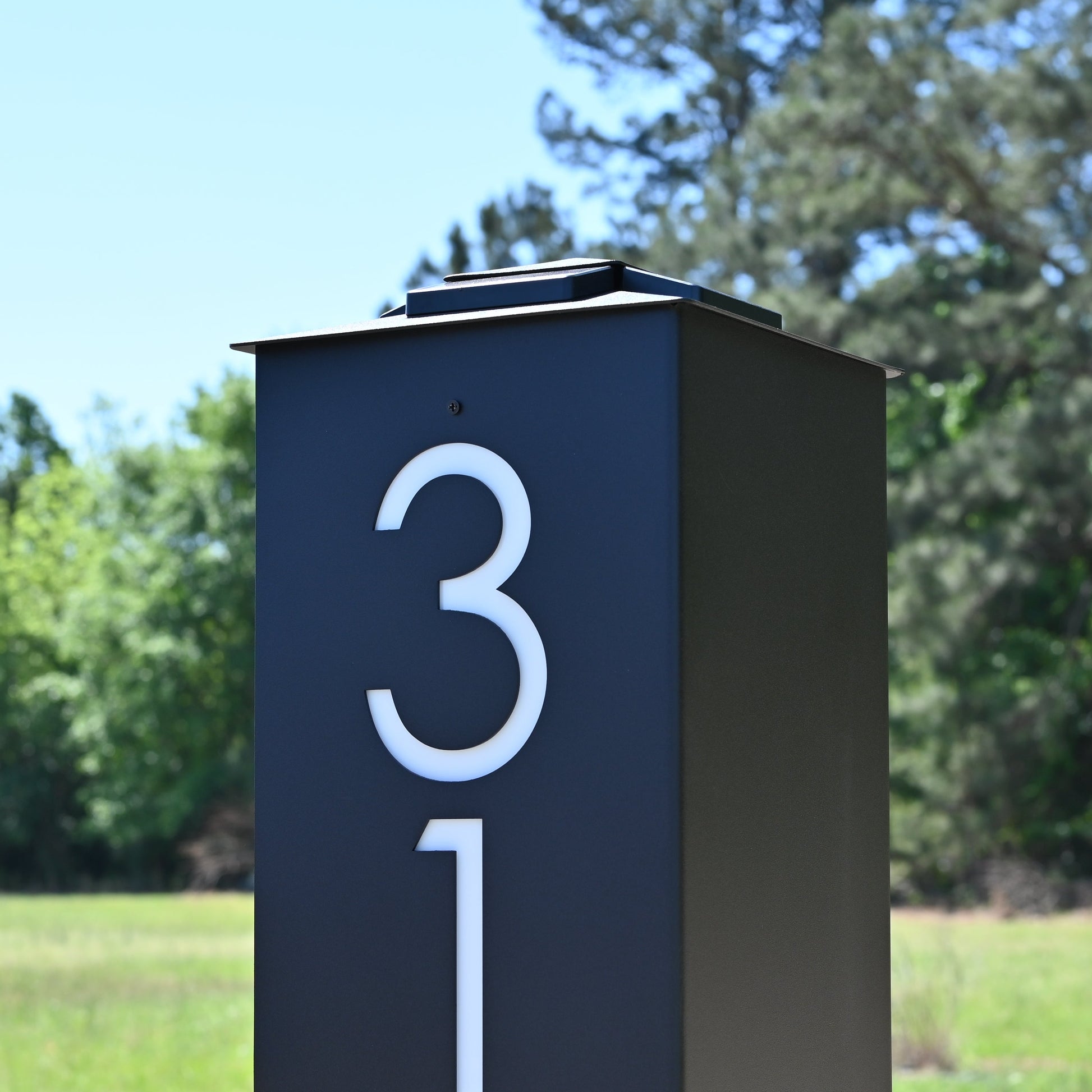 Modern mailbox with house numbers '3121' in a natural setting with trees and grass.