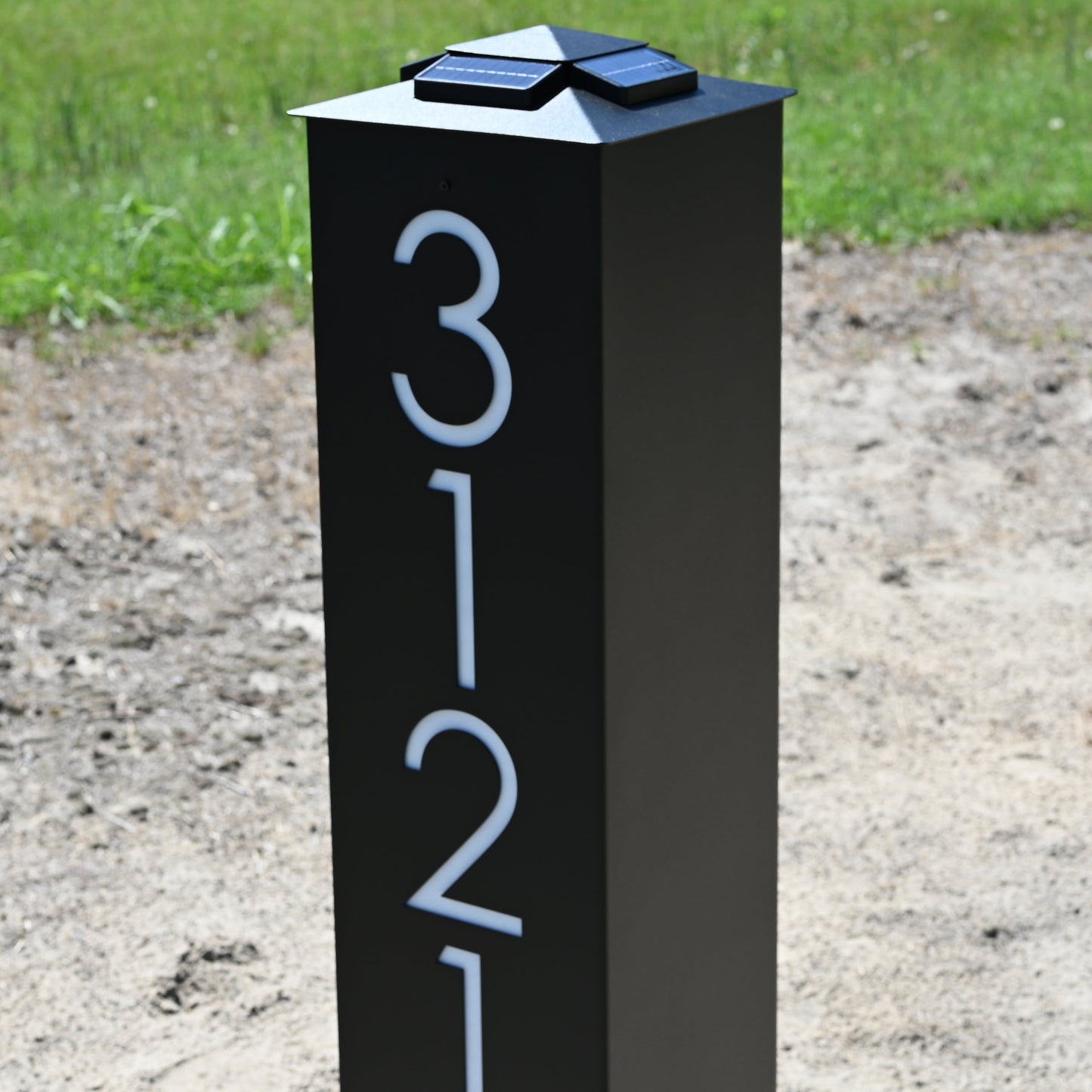 Black post with white numbers '3121' in a grassy area
