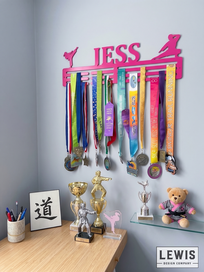 Medal holder with medals and ribbons on a wall, branded 'LEWIS Design Company'. Female Karate Medal and Award Display