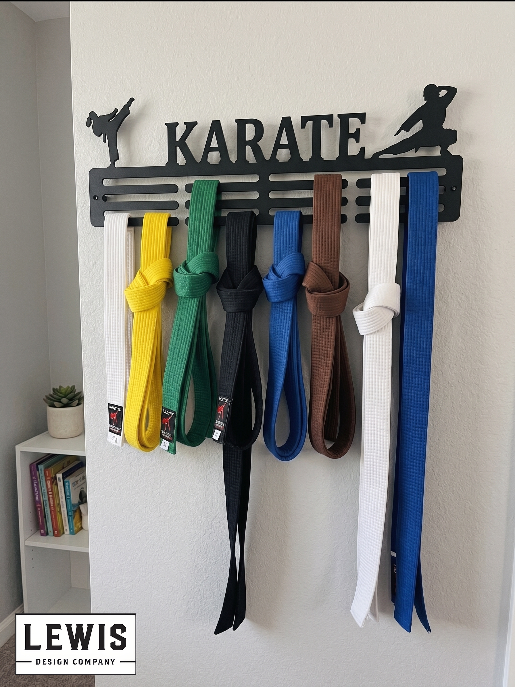 Karate belt display with various colored belts on a 'Karate' themed holder against a white wall. Medal holder with medals and ribbons on a wall, branded 'LEWIS Design Company'. Female Karate Medal and Award Display