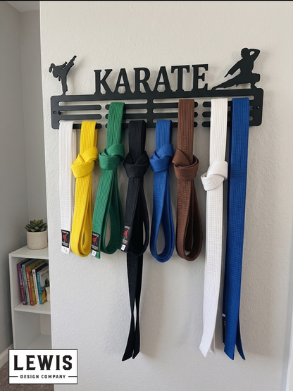 Karate belt display with various colored belts on a 'Karate' themed holder against a white wall. Medal holder with medals and ribbons on a wall, branded 'LEWIS Design Company'. Female Karate Medal and Award Display