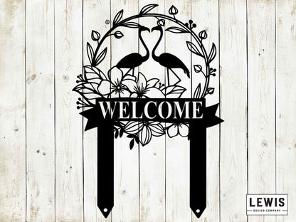 Decorative metal sign with 'WELCOME' and flamingo design on a wooden background, featuring the brand 'LEWIS Design Company'.