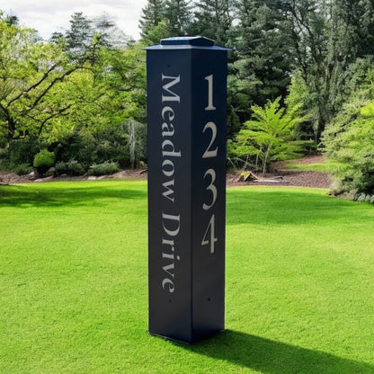 Black address signpost with 'Meadow Drive' and numbers on a grassy lawn with trees in the background