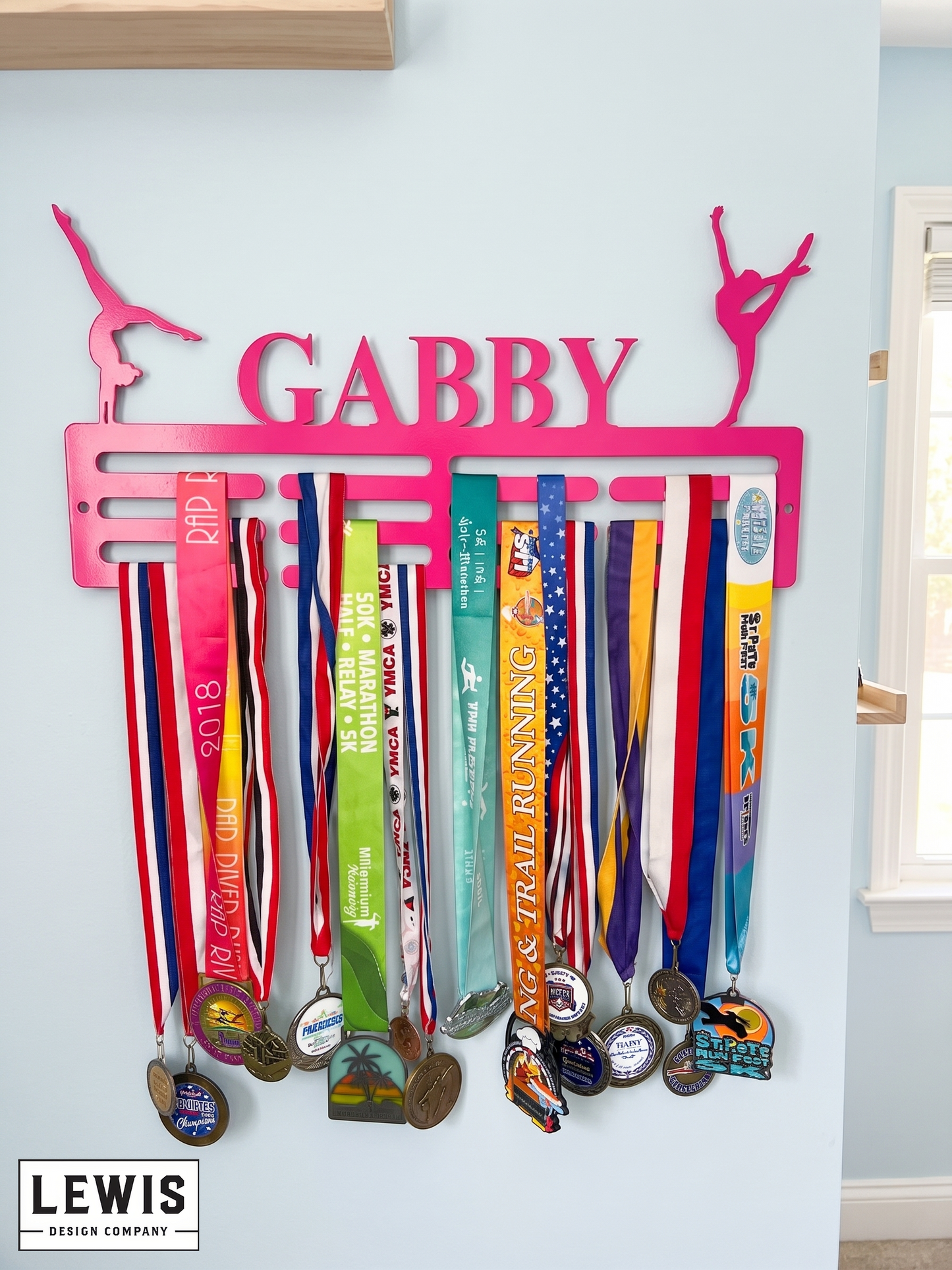 Pink medal hanger with medals and ribbons on a light blue wall, featuring the name 'Gabby' above. Gymnastics Medal Hanger