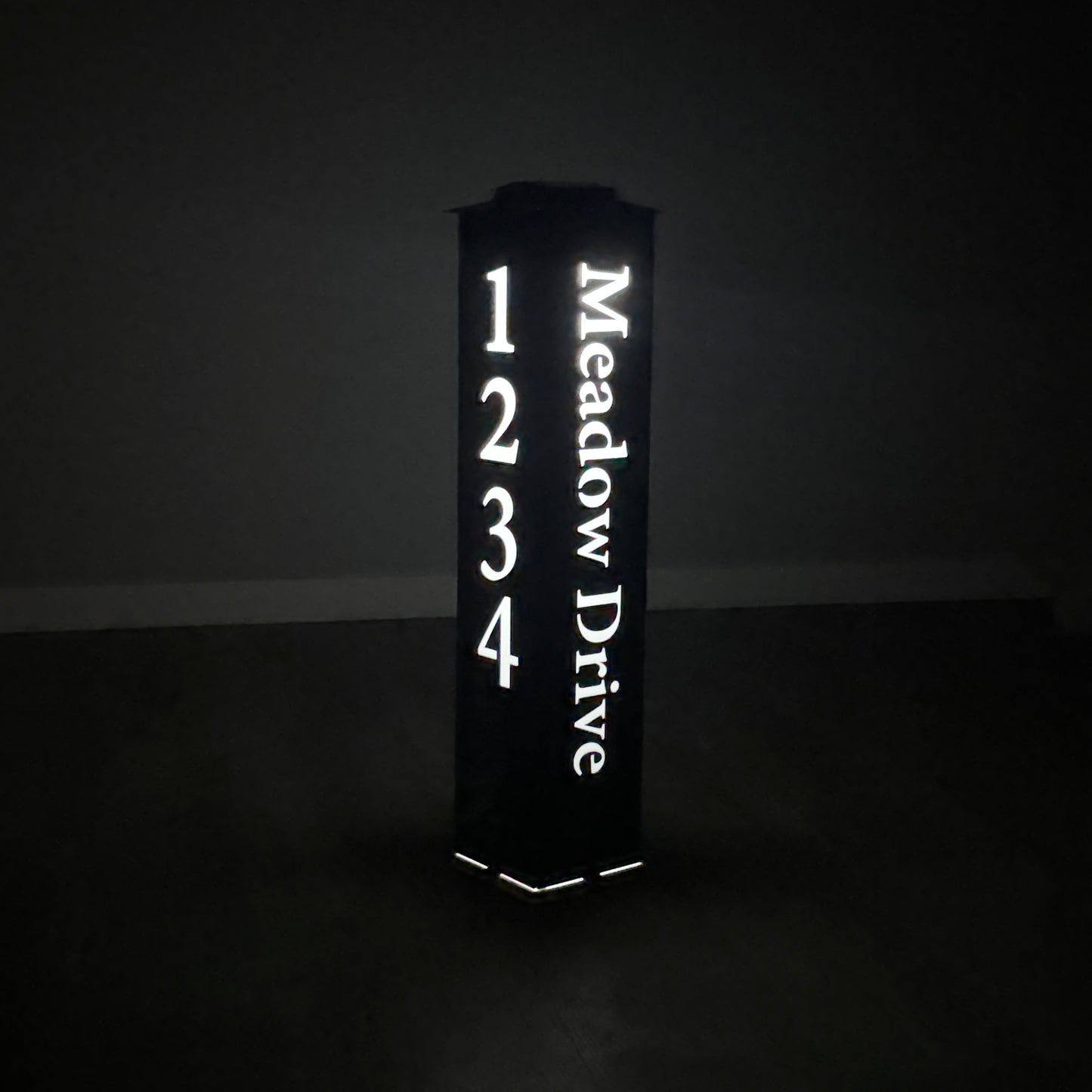 Address post sign reading 'Meadow Drive' with numbers glowing in the dark