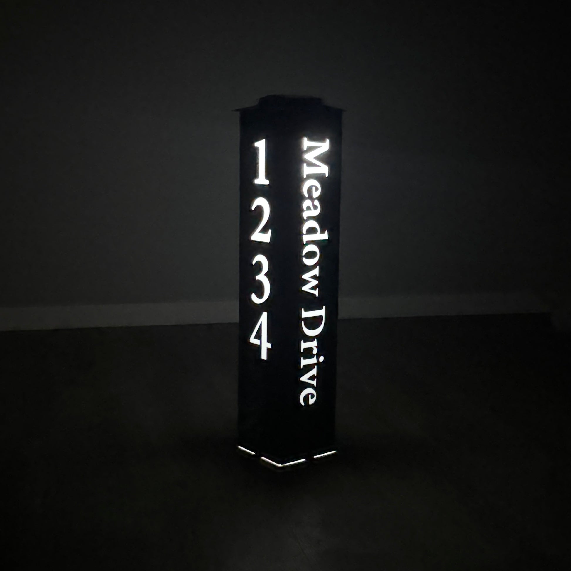 Address post sign reading 'Meadow Drive' with numbers glowing in the dark