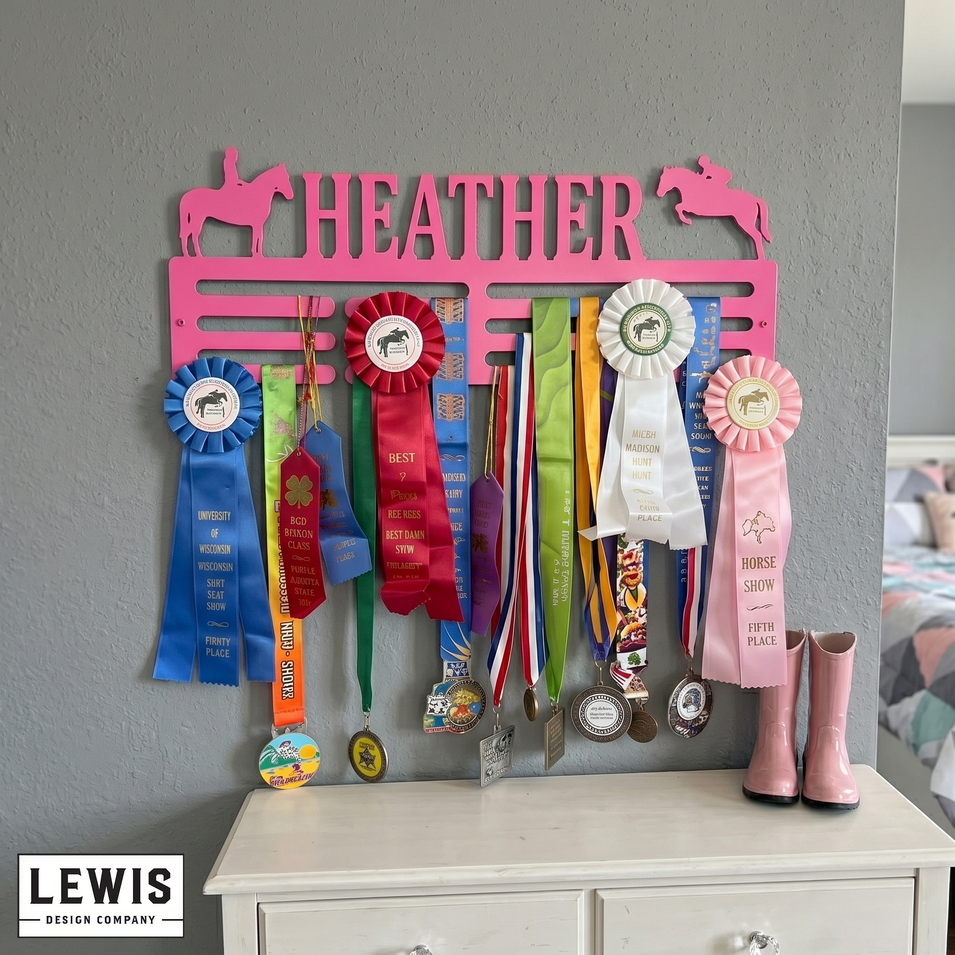 Pink medal and ribbon holder with 'HEATHER' on a gray wall above a white dresser.