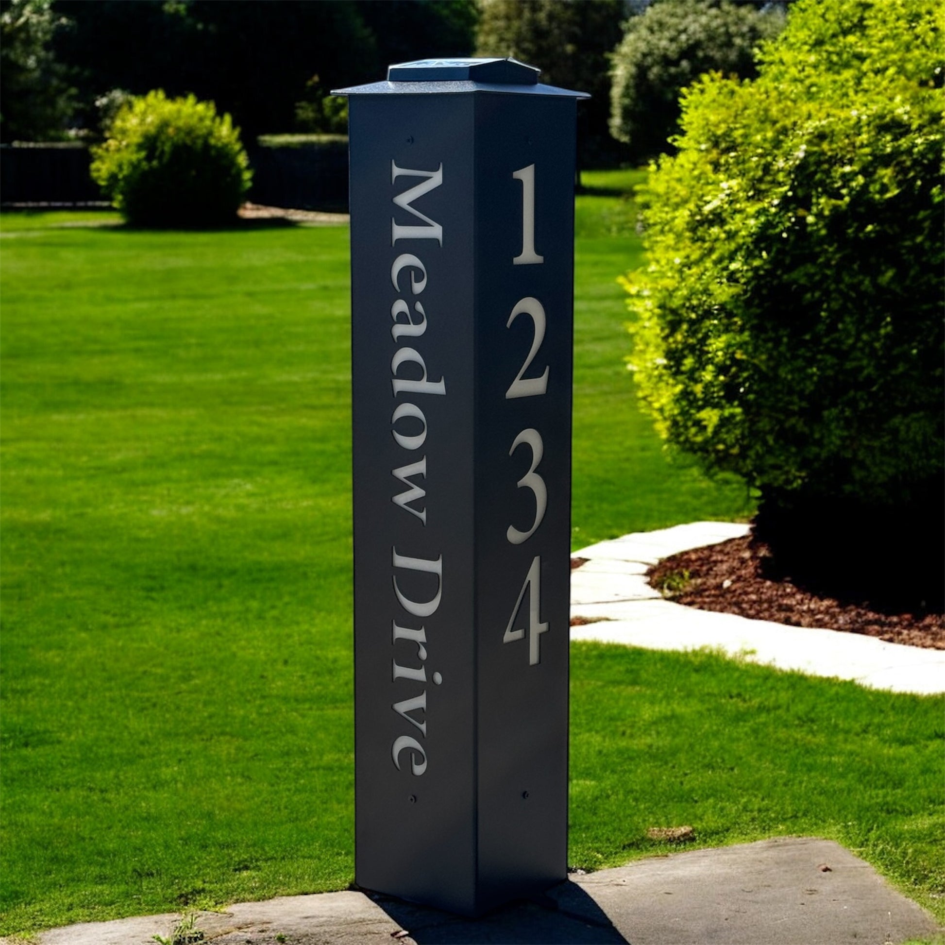 Black address signpost with 'Meadow Drive' and numbers on a grassy lawn.