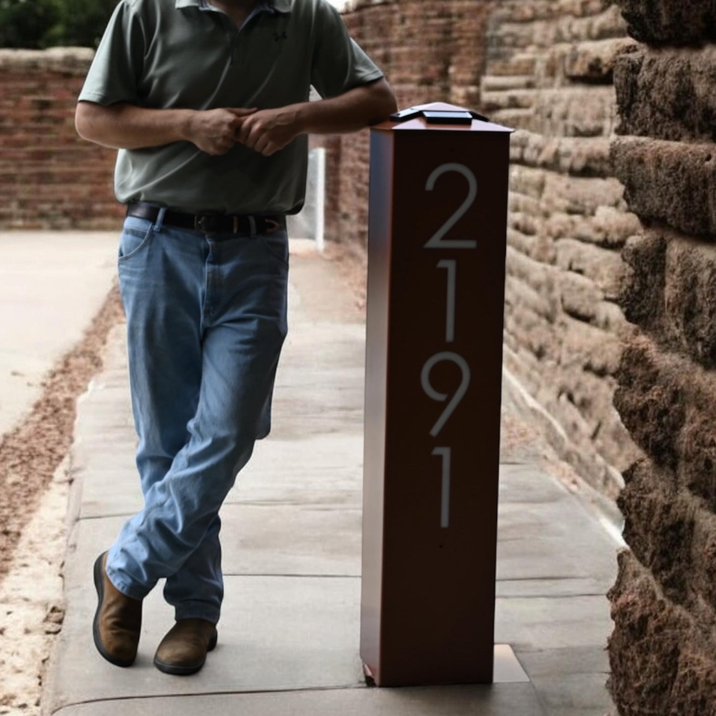 Man standing next to a brick wall with a post displaying the number 2191.