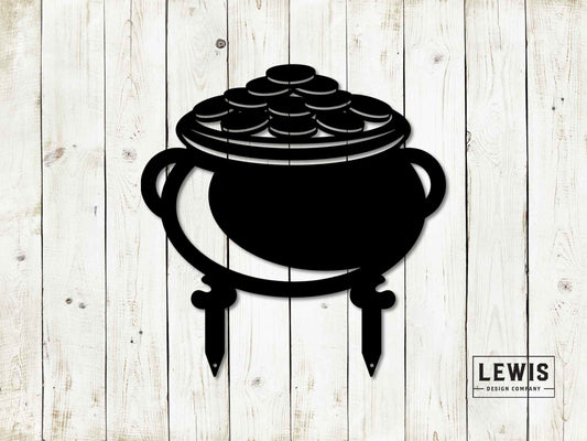 Black metal pot of gold yard stake silhouette with gold coins inside, designed for St. Patrick's Day, against a wooden background.