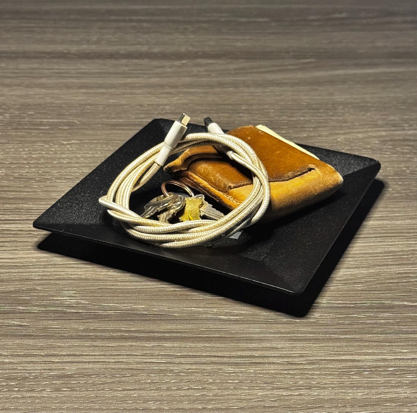 Brown leather wallet with white cable on a black square platform on a wooden surface
