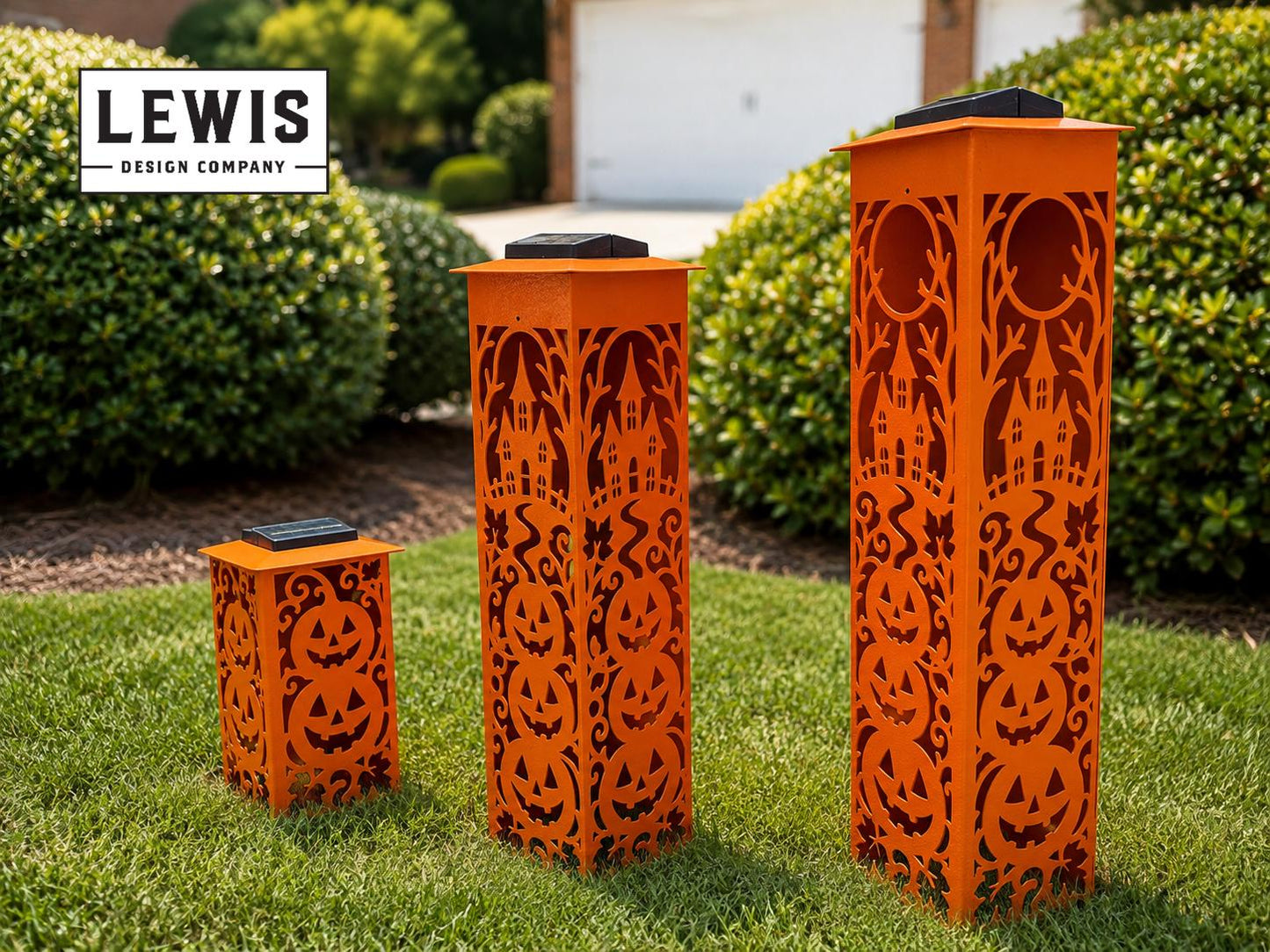 Three orange laser-cut metal Halloween yard lights of different heights, featuring jack-o'-lantern and haunted house patterns, displayed on a green lawn with a 'LEWIS DESIGN COMPANY' logo in the top-left corner.