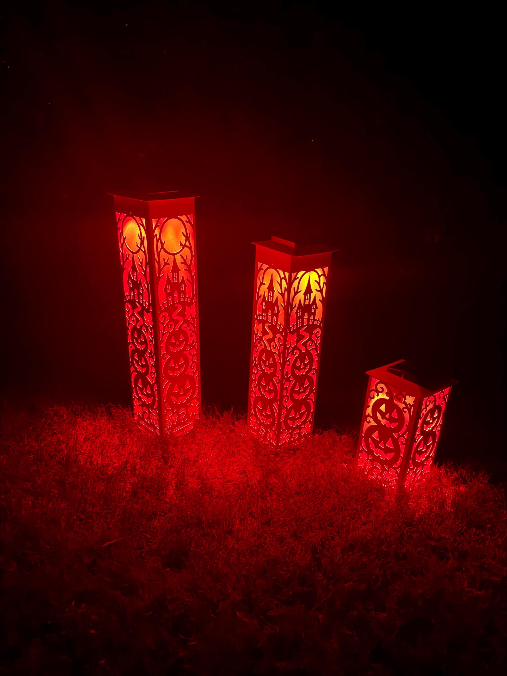 Three red decorative metal lanterns with intricate cutout patterns, glowing with warm light on a dark background.